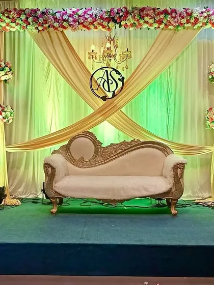 A vibrant stage setup featuring a unique crisscross drape in gold fabric against a green-lit backdrop. The design is accented with a custom monogram, a classic chandelier, and floral bouquets, offering a colorful yet elegant option.