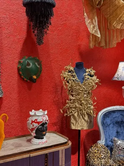 A curated collection of objects in the 'Bad Taste?' installation, where a decadent blue armchair sits against a textured red wall. The space captures an alternate visual sensibility, using audacious forms and over-the-top artworks to challenge accepted notions of taste.
