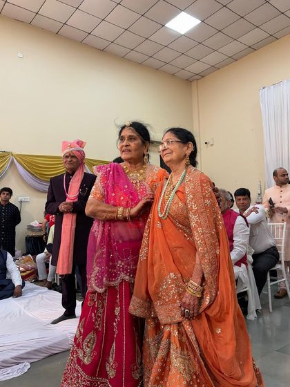A candid moment from a wedding, featuring two family members in our custom designs. One is wearing a vibrant pink lehenga, and the other an elegant orange saree with heavy zardosi work.
