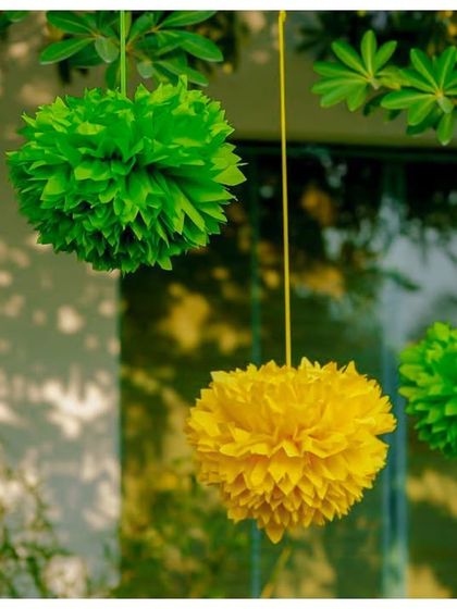 Colourful paper pom-poms in yellow and green hang from a tree, adding to the festive and cheerful atmosphere of the outdoor party.