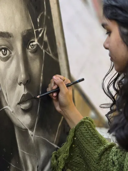 A close-up shot of an artist carefully drawing the cracks on a piece of shattered glass in her hyper-realistic charcoal portrait.