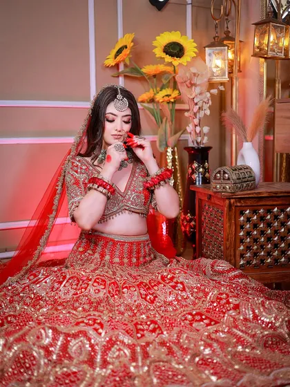 A wider shot of the bride seated, showing the full grandeur of her outfit against a decorated studio backdrop.