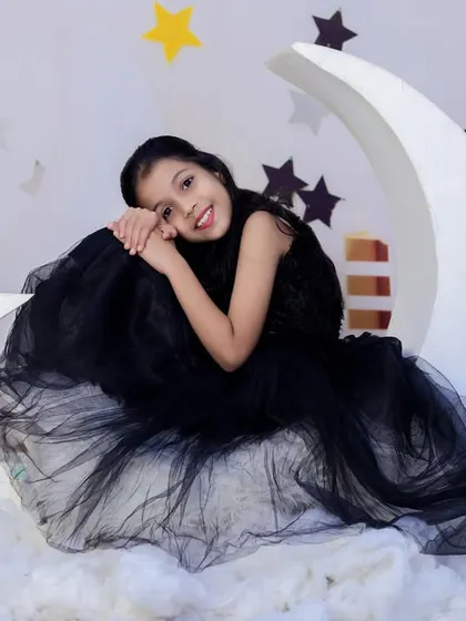 A girl in a stunning black gown poses gracefully on our moon prop, creating a dramatic and elegant portrait for an older child's birthday.