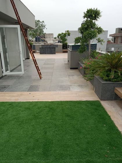 This image shows the layout of a residential terrace, combining a soft artificial grass area with granite tile flooring and built-in planters for a multi-textured look.
