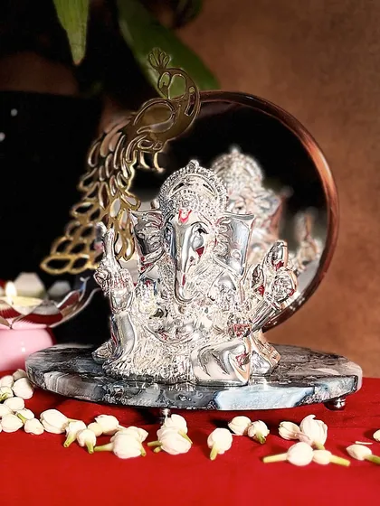 A close-up view reveals the intricate craftsmanship of the silver-plated Ganesha and the elegant peacock detail on the mirror. This idol is designed to be admired from every angle.