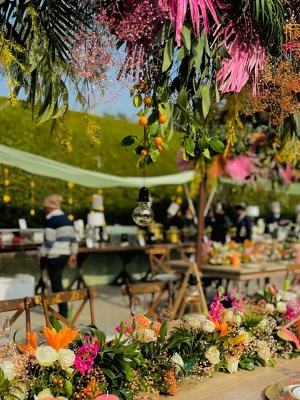 A vibrant table runner made of fresh, colorful florals and citrus fruits. The overhead installation of hanging greenery and oranges added to the fresh, summery feel of this brunch setup.