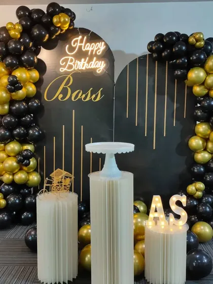 A premium black and gold birthday setup for a boss in an office setting, featuring a custom backdrop and a balloon arch.