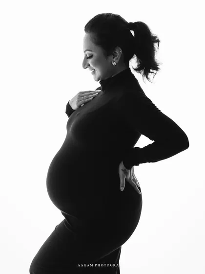 A high-key black and white maternity portrait. The bright, clean background and her joyful expression create a light, airy, and modern feel.