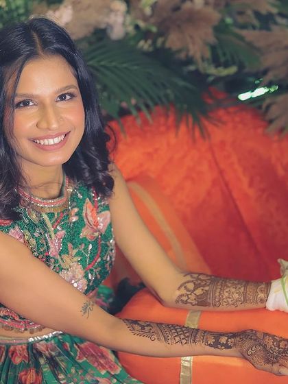 The bride smiles for the camera while her mehendi is being applied, looking radiant in her green floral outfit.