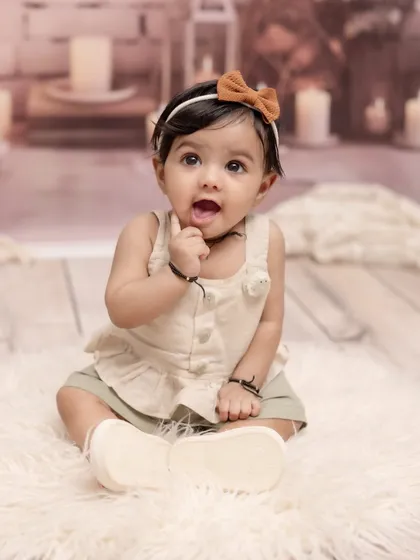 Capturing that curious and adorable sitter stage. This simple and sweet portrait of a baby girl, sitting up and exploring, focuses on her bright eyes and charming personality against a soft, neutral background.