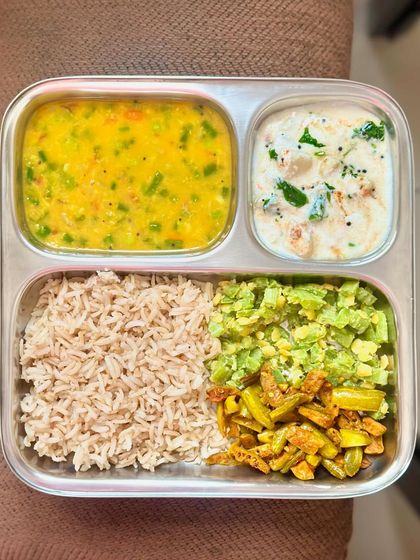 A colorful and balanced plate of brown rice, mixed vegetable dal, sautéed snake gourd and ivy gourd, and a refreshing raita.