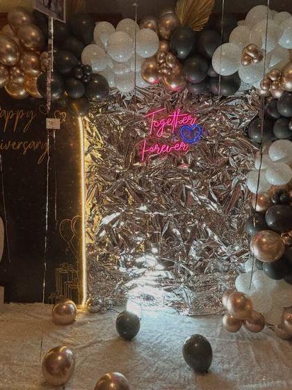 This "Bling Bling" decor is perfect for anniversaries. It features a silver foil backdrop, a "Together Forever" neon sign, and a black, white, and gold balloon arch.