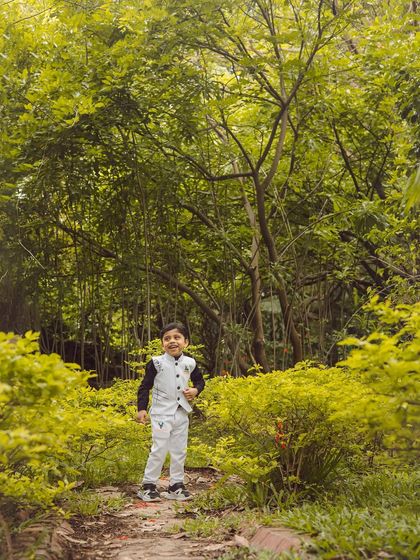 A wide shot showing the little boy standing confidently in the lush greenery. Outdoor photography allows us to capture kids in their element.