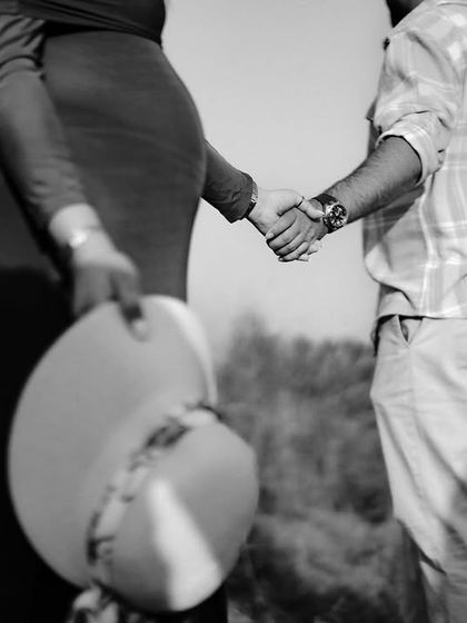 A black and white shot of the couple holding hands from behind. Her other hand holds a hat, adding a touch of style to this classic walking pose.