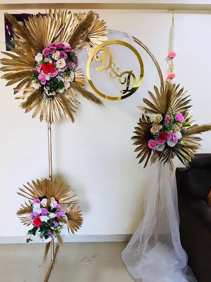 An elegant and minimalist engagement or anniversary decor piece. A golden arch is decorated with floral arrangements featuring dried golden palm leaves and a custom monogram.