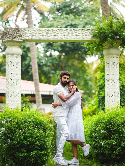A romantic portrait in front of a white stone archway, surrounded by lush greenery.