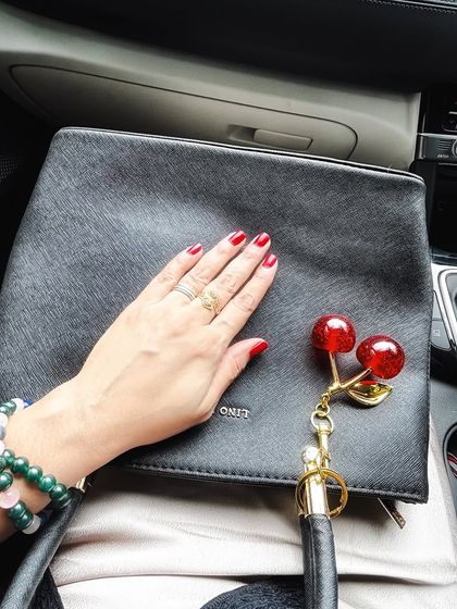 A close-up of my hand with red nails on my black handbag, showing off the cherry charm and my bracelets. It's all about the small details.