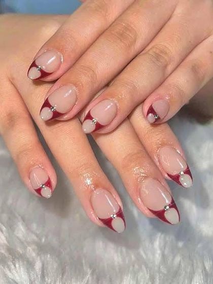 A modern and chic design with a deep red and white heart-shaped French tip, accented with a single rhinestone.