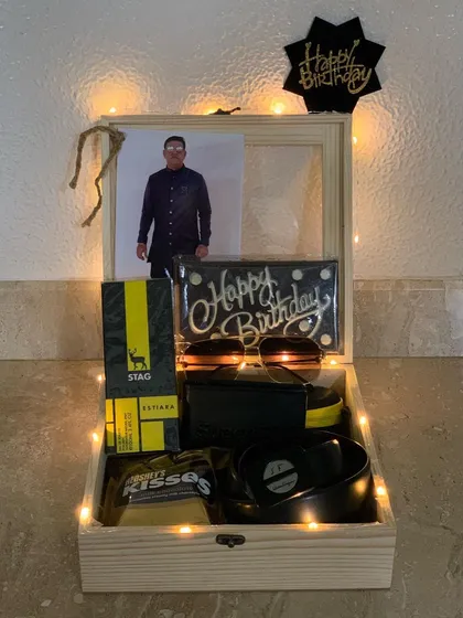 A clear, well-lit shot of the complete birthday hamper for him. The fairy lights inside the box highlight each gift, including the sunglasses, belt, and custom chocolate bar.