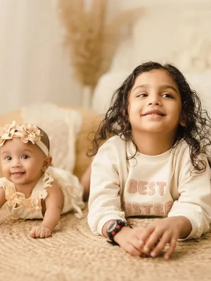 Two sisters lie side by side on a jute rug, smiling for the camera. This is a classic pose for capturing the growing friendship between siblings.
