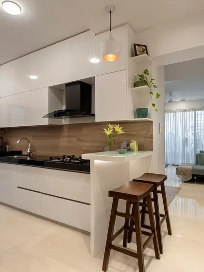 A look at one of our custom modular kitchen solutions. This design features sleek, handleless white cabinets, a contrasting wooden backsplash, and a practical breakfast bar, creating an open and inviting culinary space that is perfect for modern living.