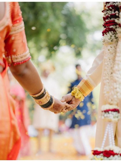 A close-up of the couple holding hands. This simple, beautiful shot focuses on their connection, the traditional bangles, and the shower of petals around them.