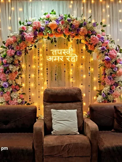 An elegant backdrop for a Jain Tapasvi ceremony. I used a beautiful arch of pastel flowers, a custom neon sign with the blessing "Tapasvi Amar Raho," and warm lighting to create a serene and respectful setting in the family's home.