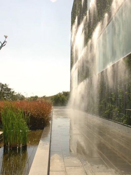 An integrated misting and irrigation system maintains the lushness of the KMC Headquarters' living facade. This image captures the system in action, a key component of the building's climate-responsive and sustainable design.