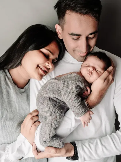 The first family portrait is always a treasure. This studio shot captures the new parents gazing lovingly at their sleeping newborn, safe in his father's hands.