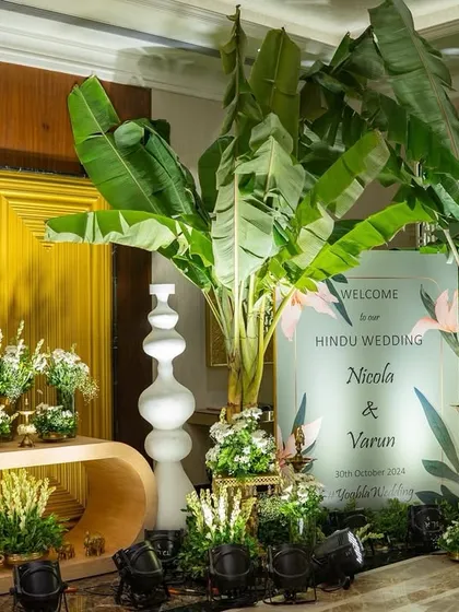 The welcome setup for Nicola and Varun's Hindu wedding. The entrance is flanked by large banana trees and modern white decor pieces, creating a beautiful fusion of contemporary and traditional design.