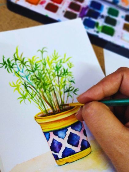 A close-up of a student painting a decorative pot with watercolors, focusing on capturing patterns and colors.