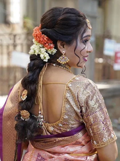The back view of a South Indian bride, showing how the pre-pleated saree complements the intricate hairstyle and blouse design. The pallu drapes cleanly over the shoulder.