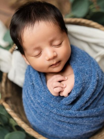 This portrait showcases the baby's beautiful dark hair and peaceful sleeping face. The simple wrap and natural elements keep the focus right where it belongs.