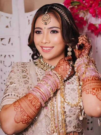 The final touches make all the difference. This bride is seen adjusting her earrings, part of a complete polki set that beautifully matches her ivory lehenga and pink bangles.
