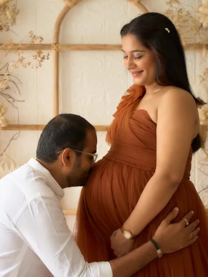A partner's gentle kiss on the baby bump. This is a classic and heartwarming pose, made even more beautiful by our Copper gown.