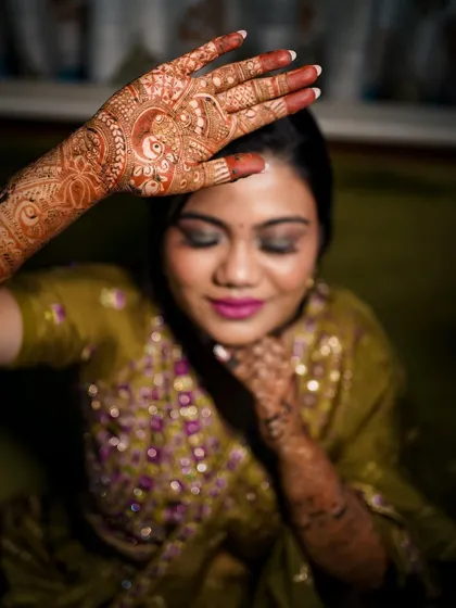 An artistic close-up of the bride's face and her intricate mehndi. The focus on the hand in the foreground creates a beautiful, layered portrait.
