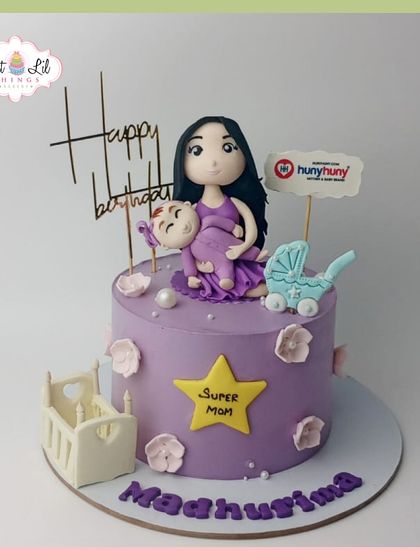 A "Super Mom" cake for Madhurima, celebrating her with a custom figurine holding her baby, surrounded by a cradle and stroller.