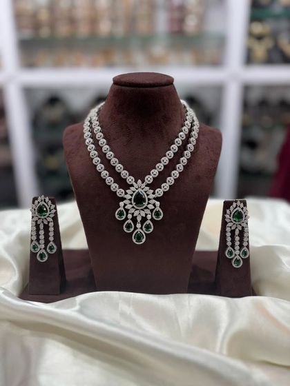 A double-layered AD necklace set with a central pendant. This versatile design comes in multiple colors including pink, white, emerald, and sapphire blue, making it a great addition to your inventory.