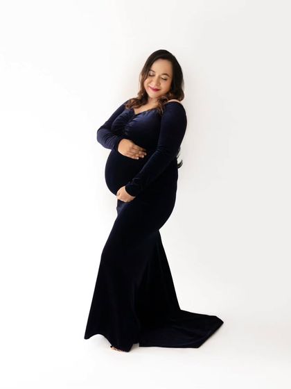 A full-length shot showcasing the elegant silhouette of the mom-to-be in a long-sleeved navy velvet maternity dress.
