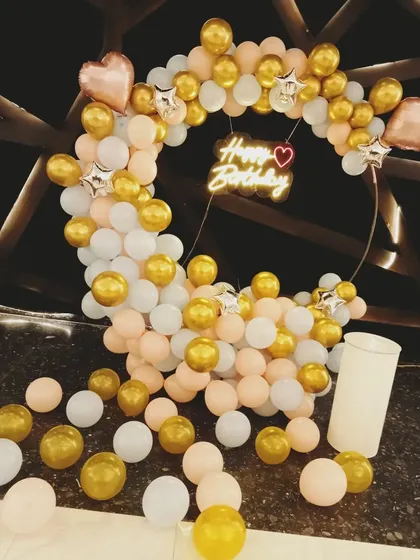 A simple yet beautiful birthday balloon ring in peach, white, and gold. The scattered balloons on the floor make the setup feel more full and festive.