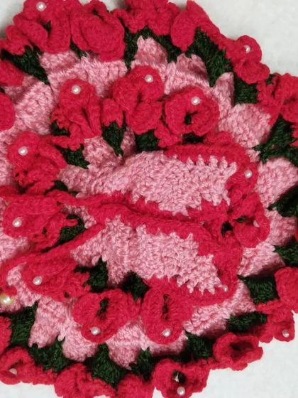 A beautiful pink woolen dress covered in dozens of tiny, hand-crocheted red roses. This intricate design is one of my favorites to make, perfect for a special occasion.
