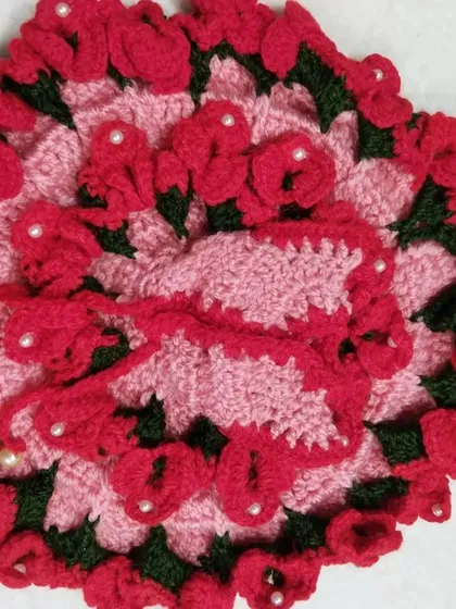 A beautiful pink woolen dress covered in dozens of tiny, hand-crocheted red roses. This intricate design is one of my favorites to make, perfect for a special occasion.
