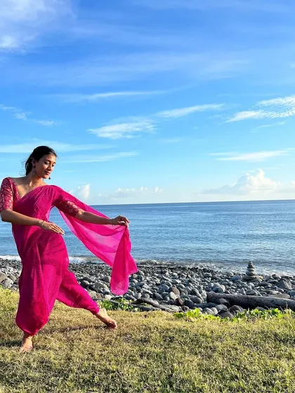 A gentle dance pose in a pink saree against the sea and sky. The soft colors and graceful posture create a serene and picturesque scene, perfect for travel or resort wear campaigns.