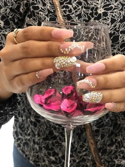 Elegance with a lot of sparkle. These coffin-shaped extensions have a soft pink glitter base, with accent nails fully covered in gold and silver rhinestones for a luxurious feel.