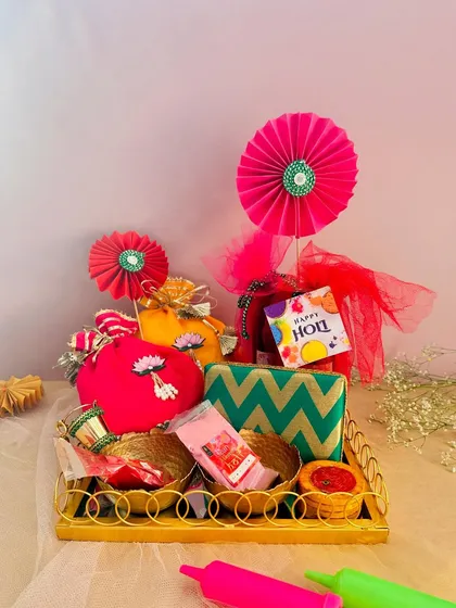 A bright and cheerful Holi hamper in a gold-painted wooden tray. The combination of red and yellow potlis with festive decorations captures the spirit of Holi perfectly.