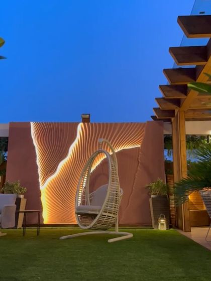 An artful accent wall with integrated lighting serves as the focal point in this terrace garden. Paired with a modern swing chair and artificial turf, it creates a stylish and low-maintenance relaxation zone.