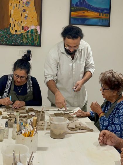A mentor provides guidance to two participants during a clay workshop, pointing out details on their handbuilt pieces.