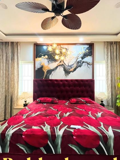 A bold and luxurious bedroom with a deep red tufted bed, a statement art piece, and a large fan.