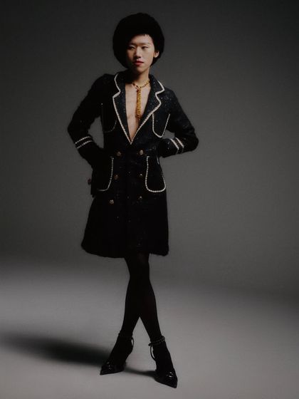 A full-length shot that captures the entire look, including the sheer tights and pointed heels. The composition is classic fashion photography, emphasizing the long lines of the silhouette.