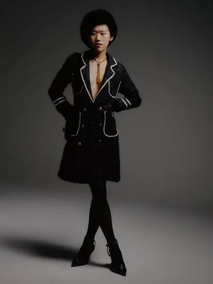 A full-length shot that captures the entire look, including the sheer tights and pointed heels. The composition is classic fashion photography, emphasizing the long lines of the silhouette.